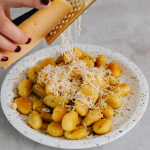Closeup of a hand grating cheese over a plate of gnocchi.