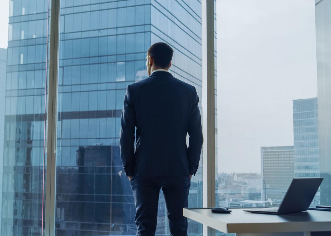 Back view of a CEO wearing a suit, standing in his office, looking out the window. 