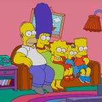 Homer, Marge, Lisa, Maggie, and Bart Simpson sit on their couch watching TV on "The Simpsons"