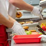 Closeup of fast food workers making burgers in kitchen.