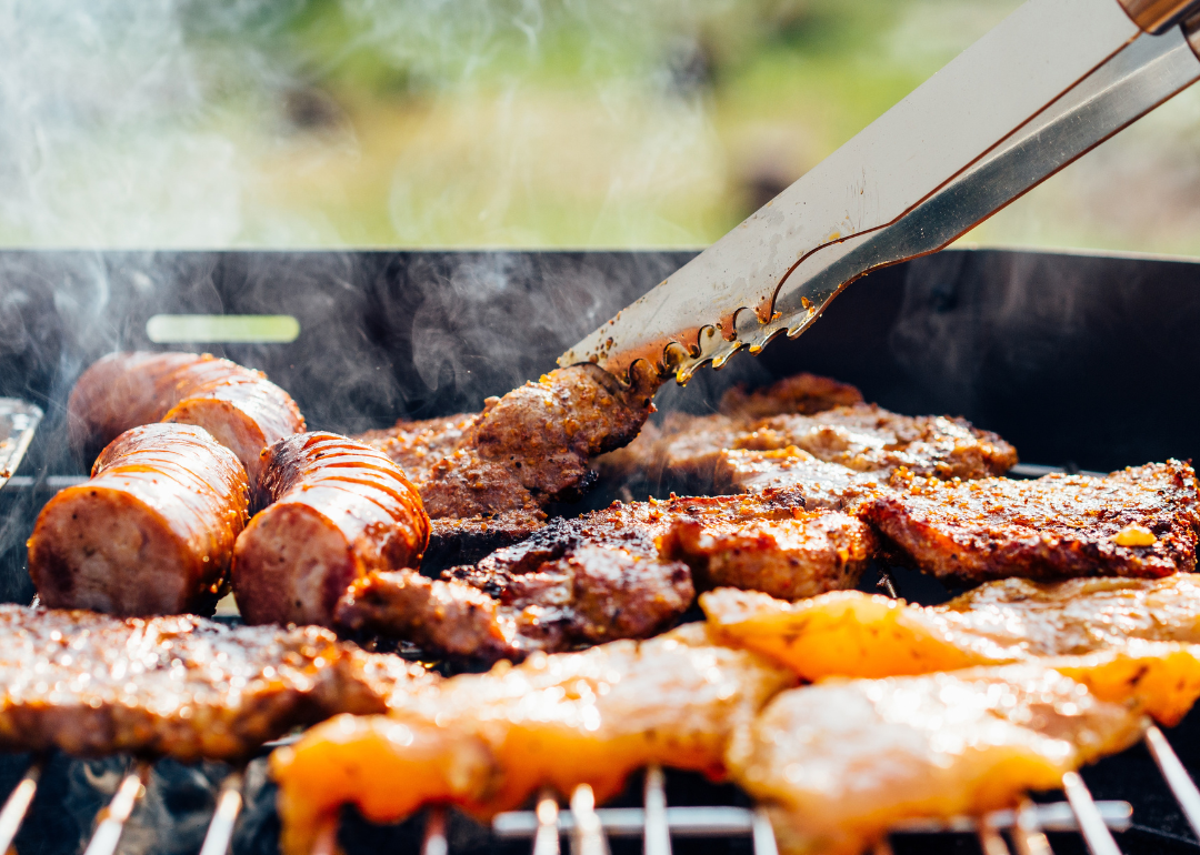Closeup of tongs flipping meat on a grill