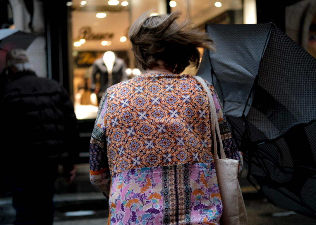 Woman photographed from behind as the wind blows her hair and her umbrella.