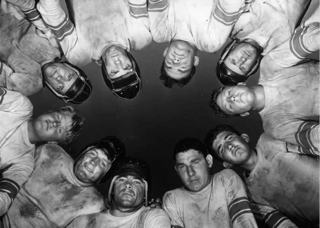 Football players in a huddle look at camera on the ground in vintage photo.