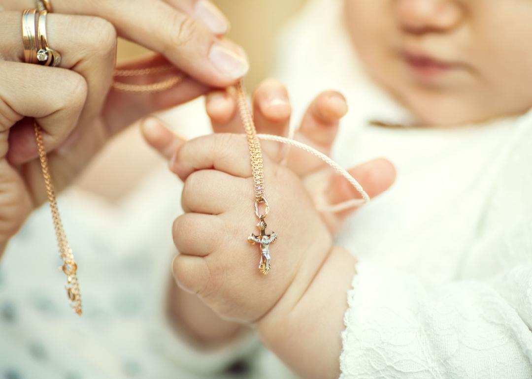 Closeup of parent and baby's hands with a cross necklace at a christening