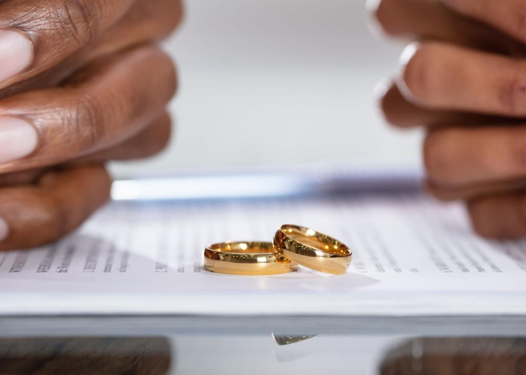 Closeup of couples' hands folded with divorce papers and their wedding bands sitting between them.