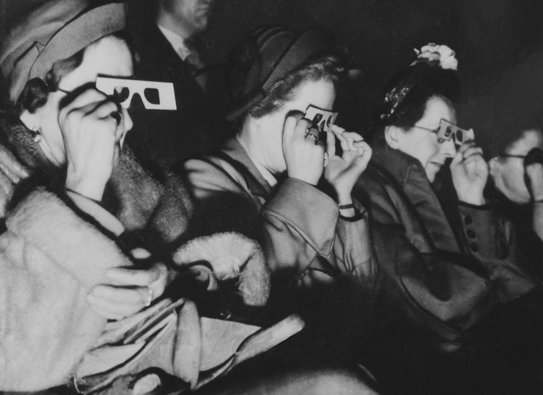 Women sitting in a cinema watching a 3D film, circa 1940s. They are holding special 3D glasses up to their eyes.