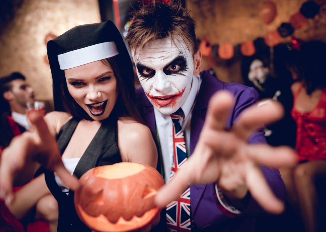 A guy in a Joker costume and a girl in a nun costume posing with a pumpkin-lamp.