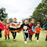 Little kids running through the grass dressed up at a Halloween party