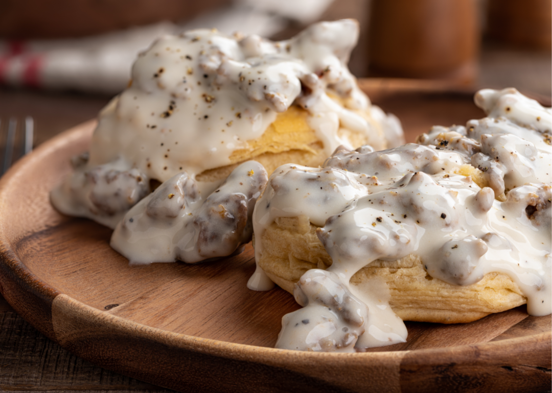 Biscuits on a wooden plate with creamy sausage gravy.