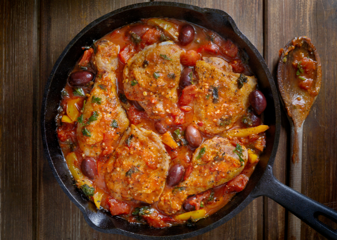 Chicken cacciatore in a cast iron skillet with a wooden spoon beside it