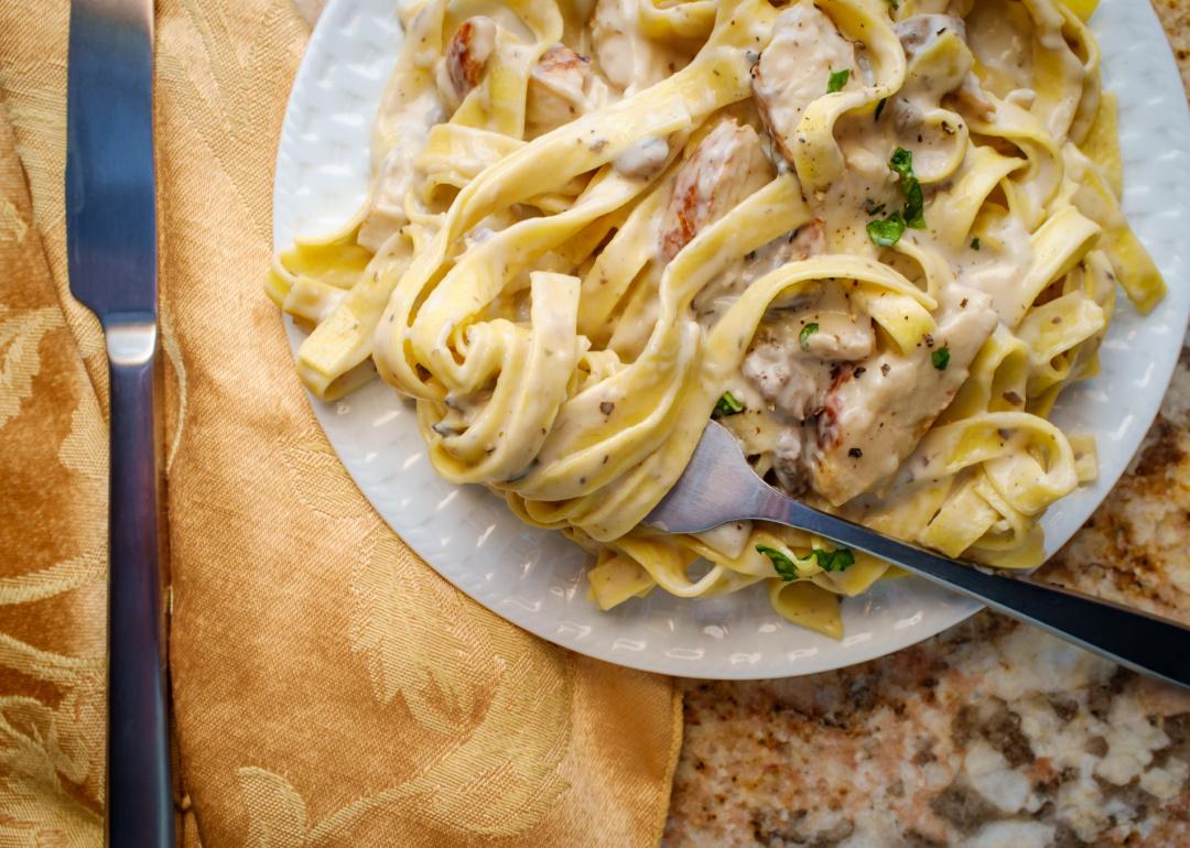 Italian fettuccine alfredo pasta dish with grilled chicken breast in a white dish on a table cloth.
