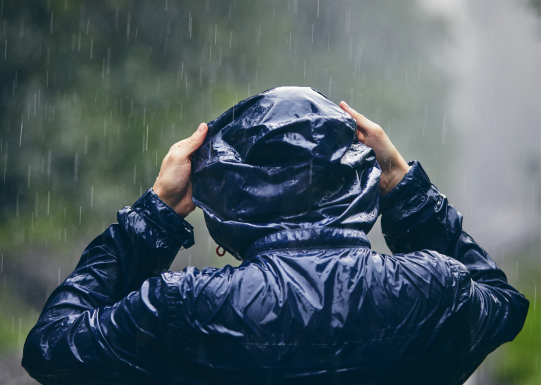 Person holds the hood of their navy blue jacket during a heavy rainstorm.