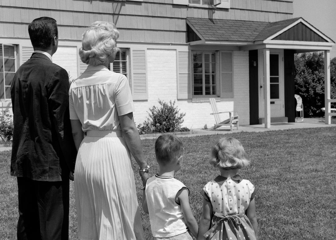 A family of four standing together looking at a suburban house in the 1950s.