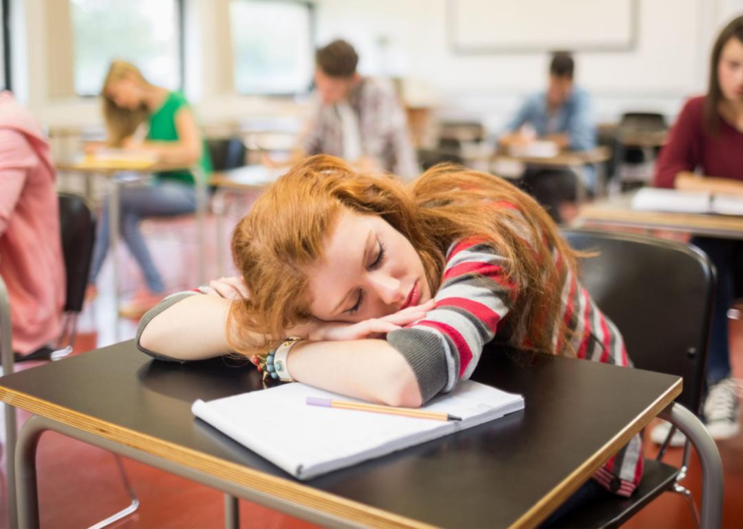 A teenage girl sleeps at her desk in a classroom