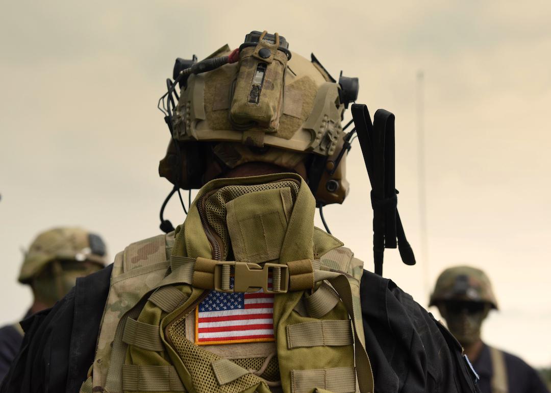 US soldier in a helmet photographed from behind with an American flag on their backpack.