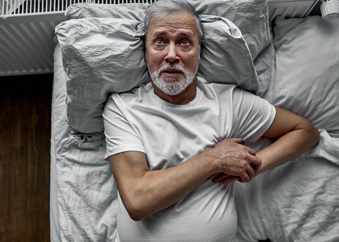 An elderly person in bed clutches their chest after waking up from a hypnic jerk in bed.