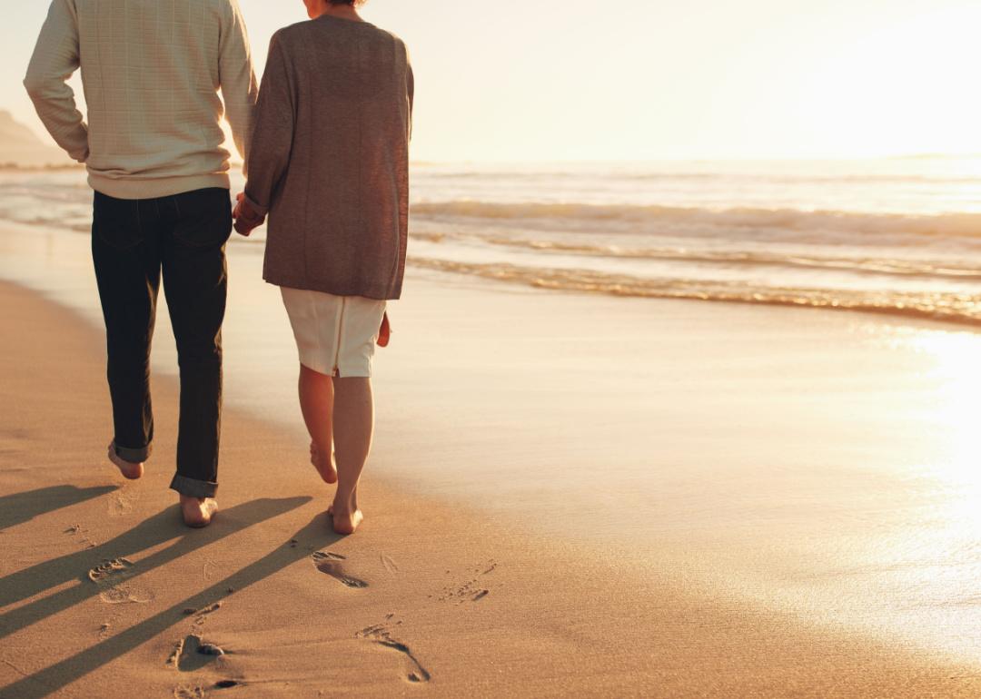 Senior couple holding hands while walking on the beach.
