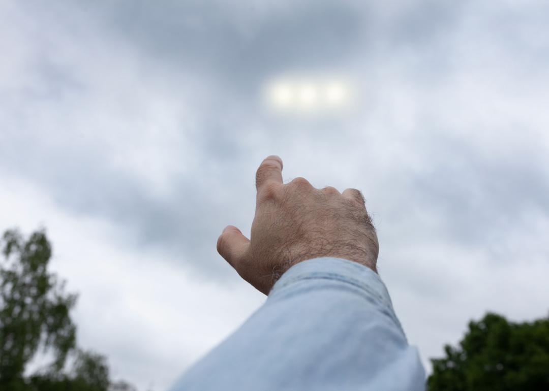 A person pointing their finger at three strange light orbs among the clouds in the sky.