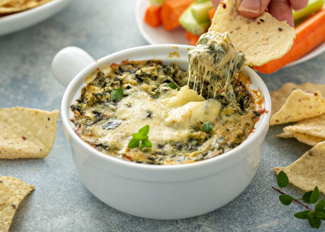 Person dipping in a chip into cheesy artichoke spinach dip.