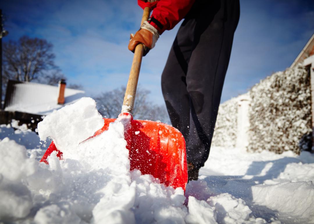 Person shoveling snow off sidewalks with a red shovel.