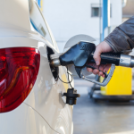 Driver filling up gas tank of white car at gas station.