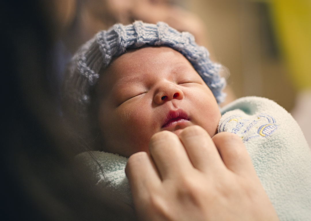 Sleeping newborn baby wearing a blue knit cap and wrapped in a green blanket.