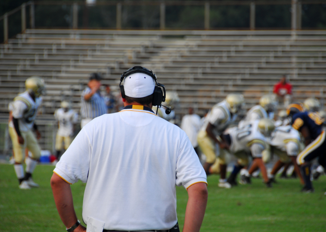 A football coach watches players on the field.
