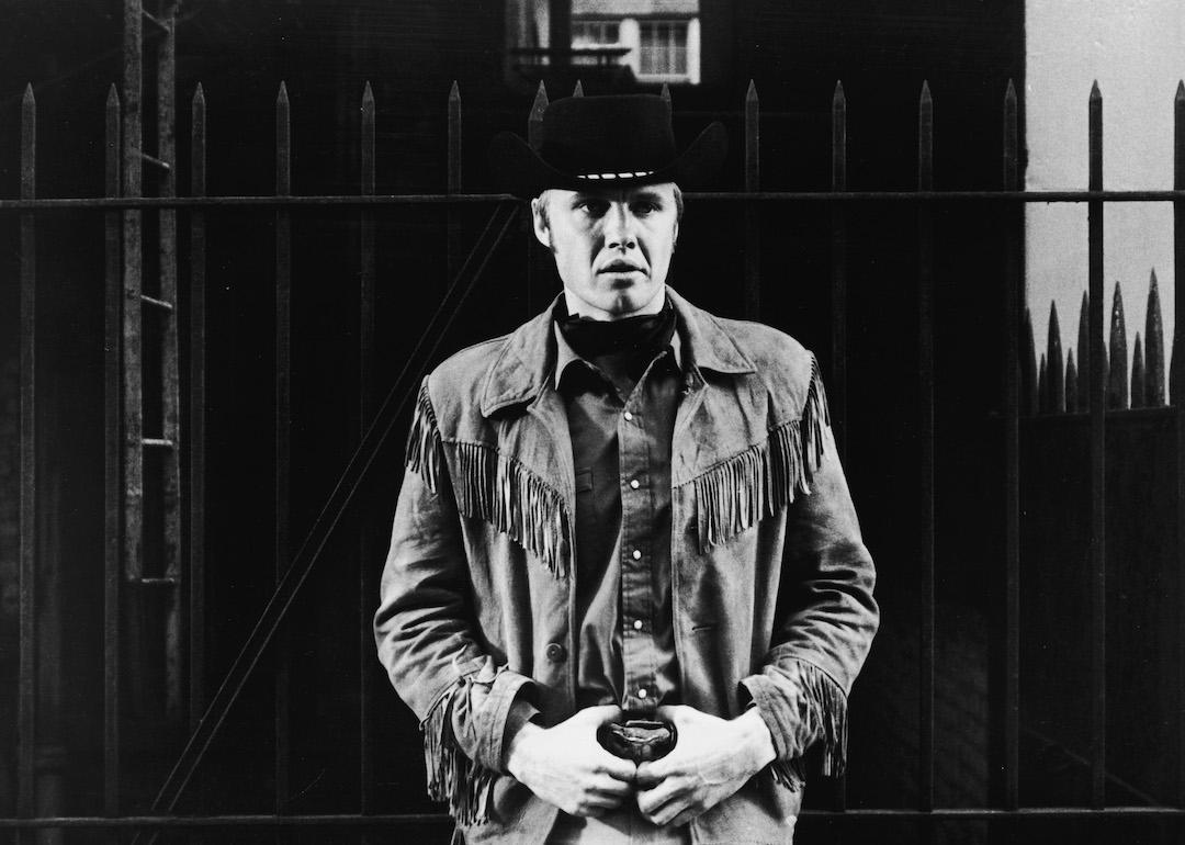 Actor Jon Voight leans against an iron fence in a still from the 1969 film 'Midnight Cowboy.'