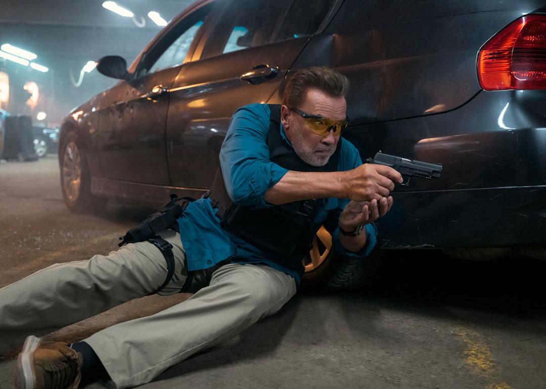 Arnold Schwarzenegger wields a weapon behind a car in the Netflix series 'FUBAR.'