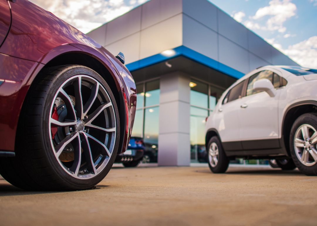 A red and a white car in front of an auto dealership.