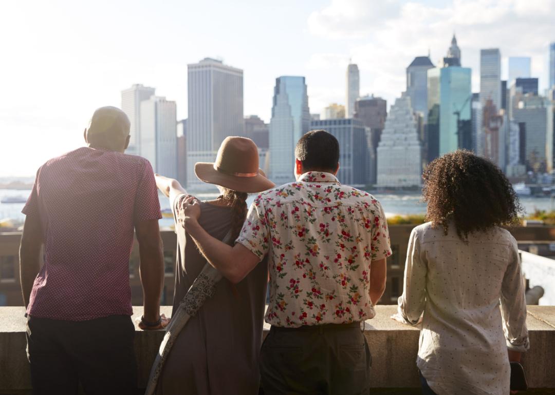 Four people looking at the Manhattan skyline, photographed from behind.