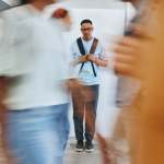 A young person stands still in a corridor and blurred images indicate others moving around them.