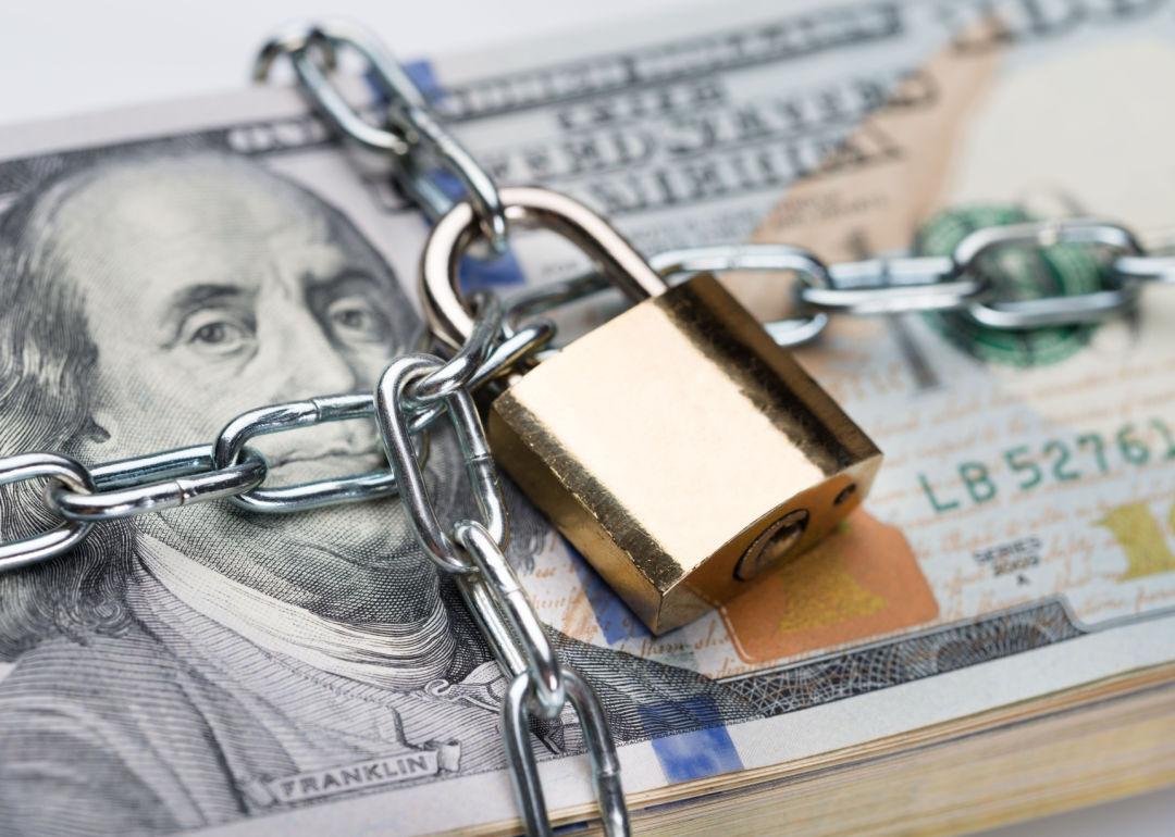 A padlock locks chain around a stack of $100 dollar bills