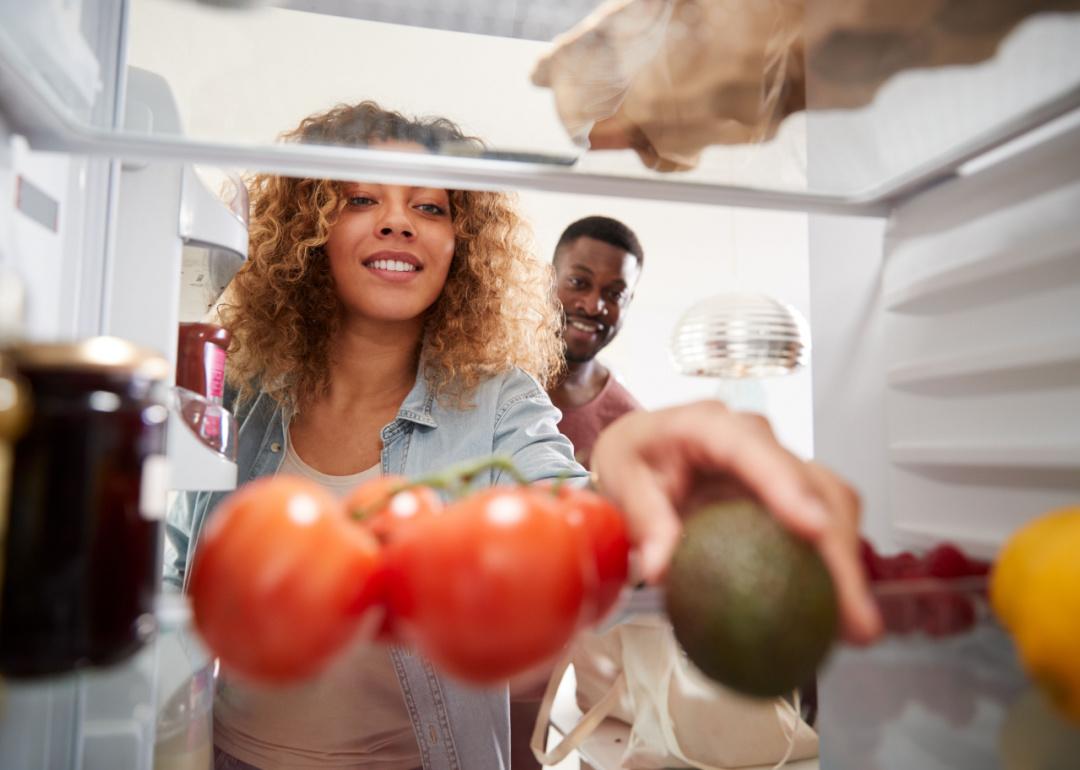 View from inside of a refrigerator as a couple puts groceries away.