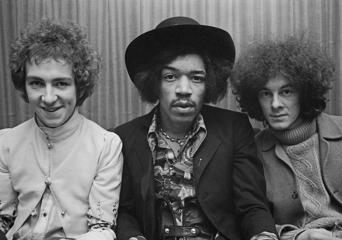 Guitarist and singer Jimi Hendrix seated in the center with his Jimi Hendrix Experience bandmates—drummer Mitch Mitchell on the left and bassist Noel Redding on the right. They were photographed in London circa August 1967.
