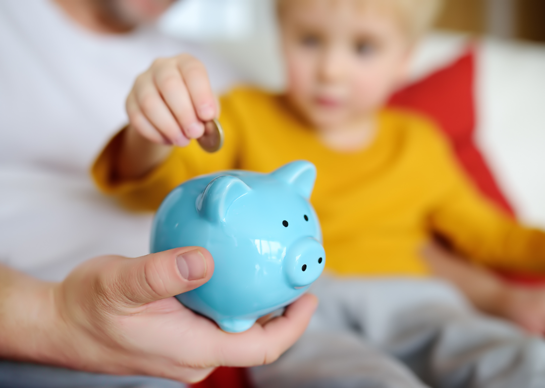 A child places a coin in a piggy bank held by a parent.