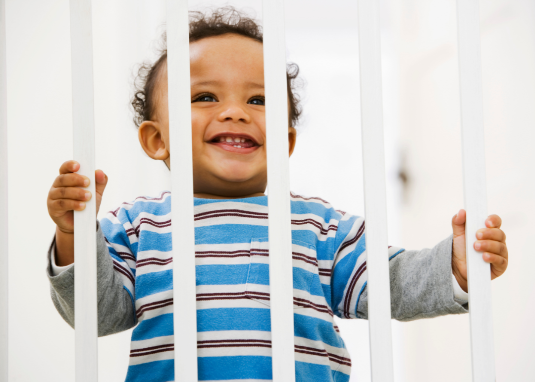 Grinning baby standing behind baby fence.