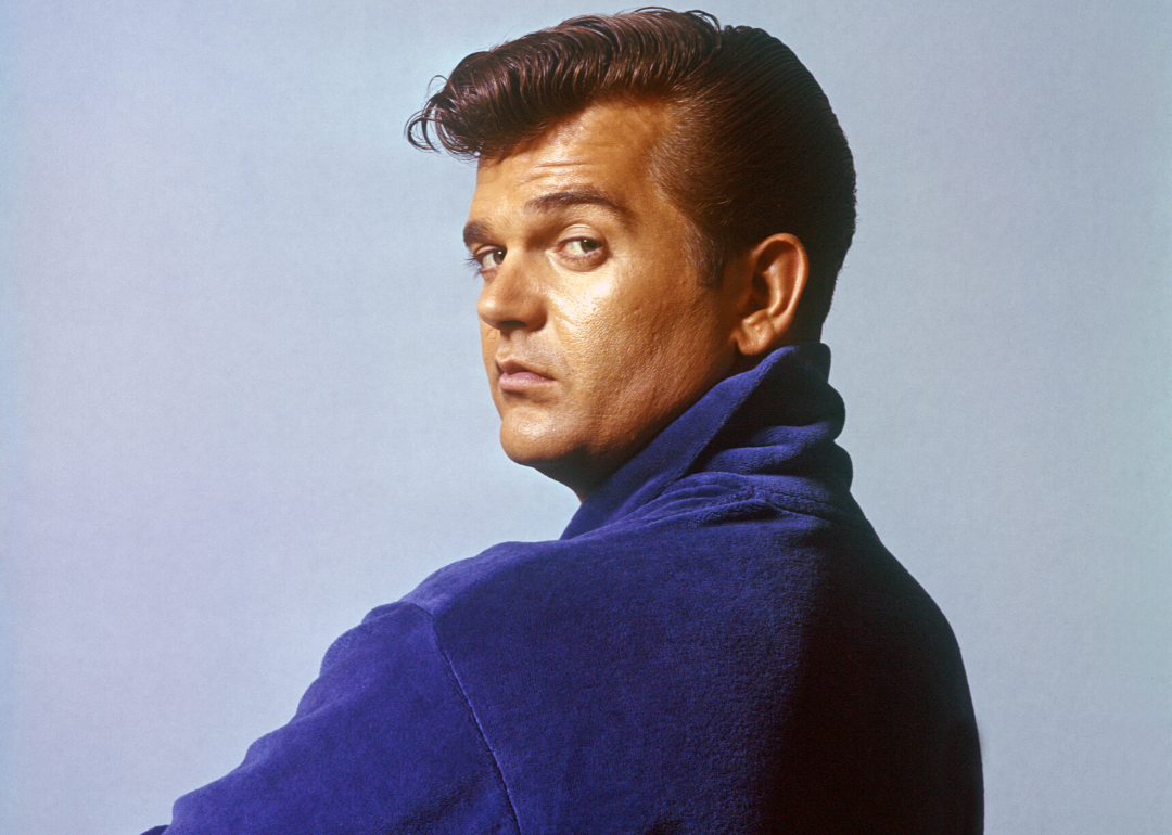 Country singer Conway Twitty looks over his shoulder while wearing a blue shirt.