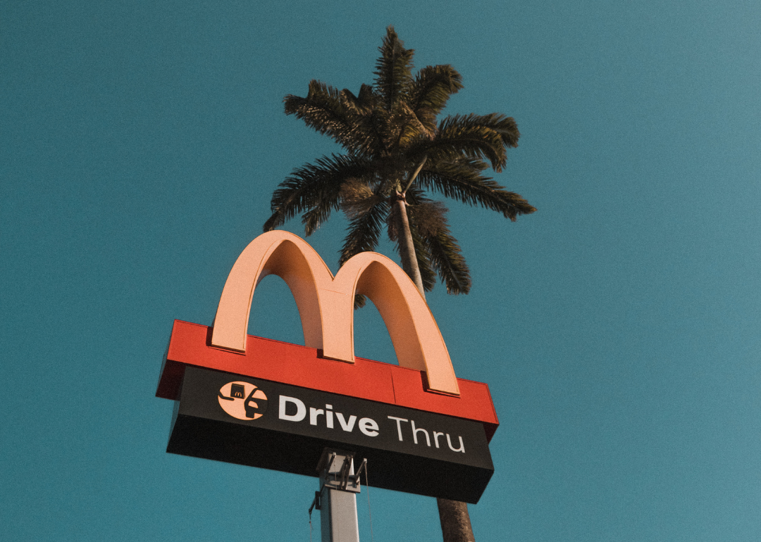 McDonald's drive-thru sign in front of a palm tree on a clear blue day.