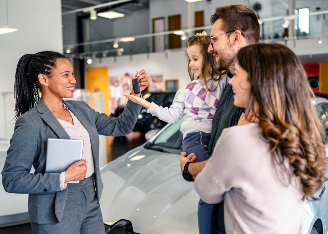 A car dealership salesperson hands keys to a young family. 