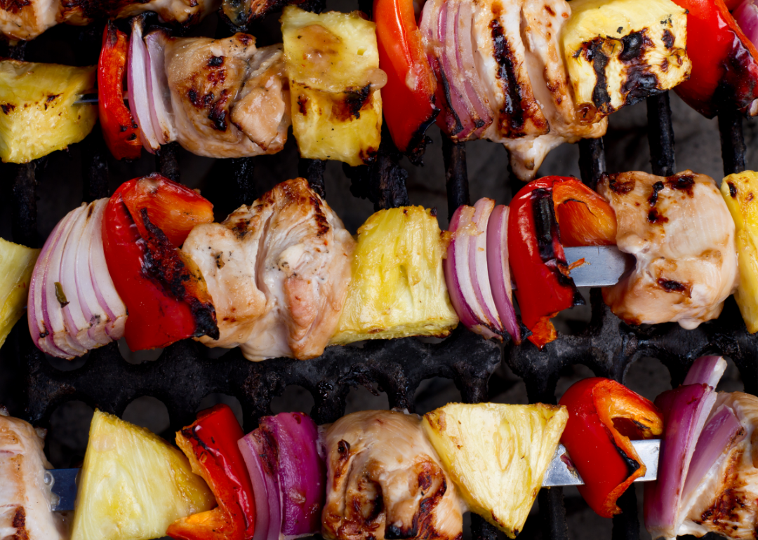 Chicken, red bell pepper, red onion, and pineapple on kabobs on the grill.