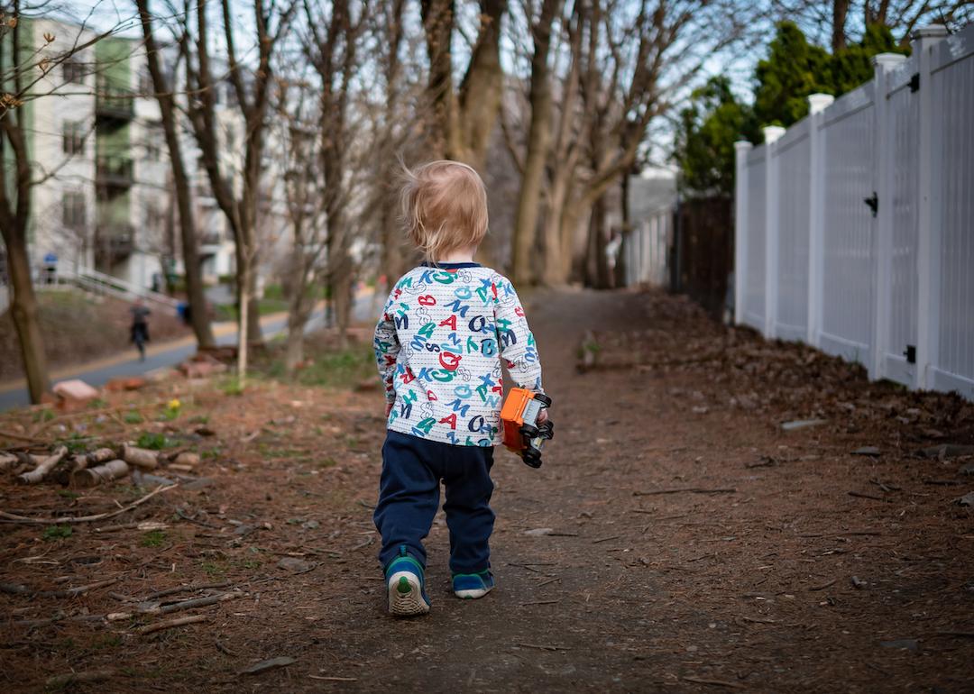 Toddler with a toy truck in his hand walking along a public community path in Somerville, Massachusetts.