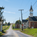 A rural American small town with a two-lane paved road and a church steeple.