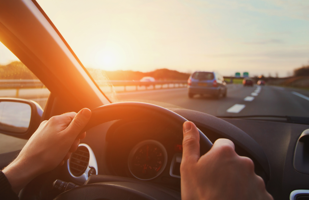 Hands of driver on steering wheel in a car driving down the highway.