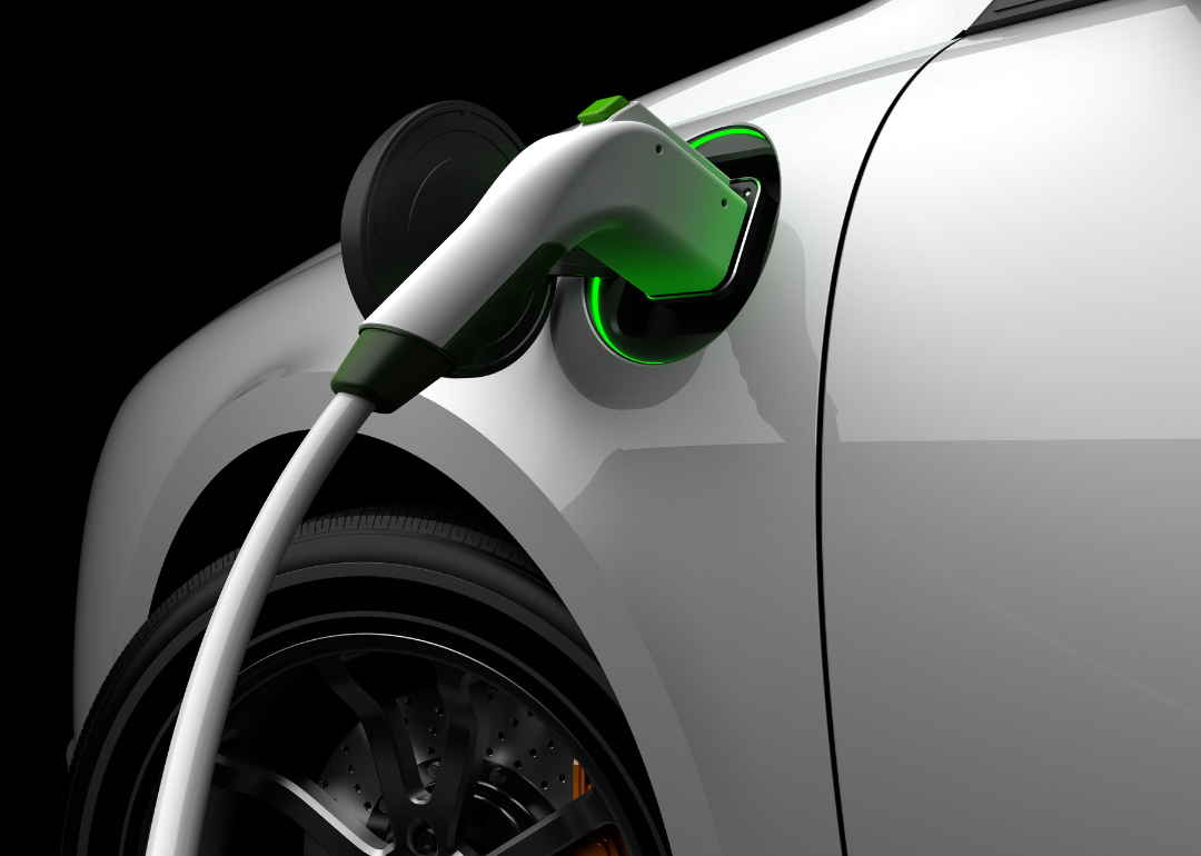 A silver-white electric vehicle being charged by an electric charge plug, silhouetted by a green light.