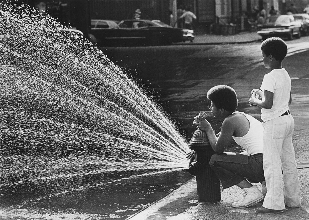 Harlem, New York: A teenager and a younger chlid stand near the sprinkler of an open fire hydrant in July, 1977.