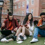 A group of three multiethnic students sit together on a college quad