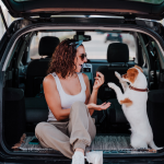 A woman and dog sit in the open rear cab of an SUV, playing.