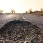 Pothole at foreground of image on an open road.