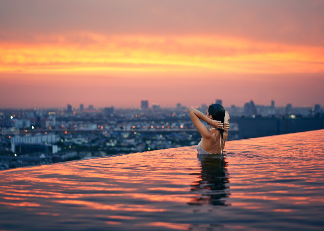 A woman stands in a rooftop pool at sunset.